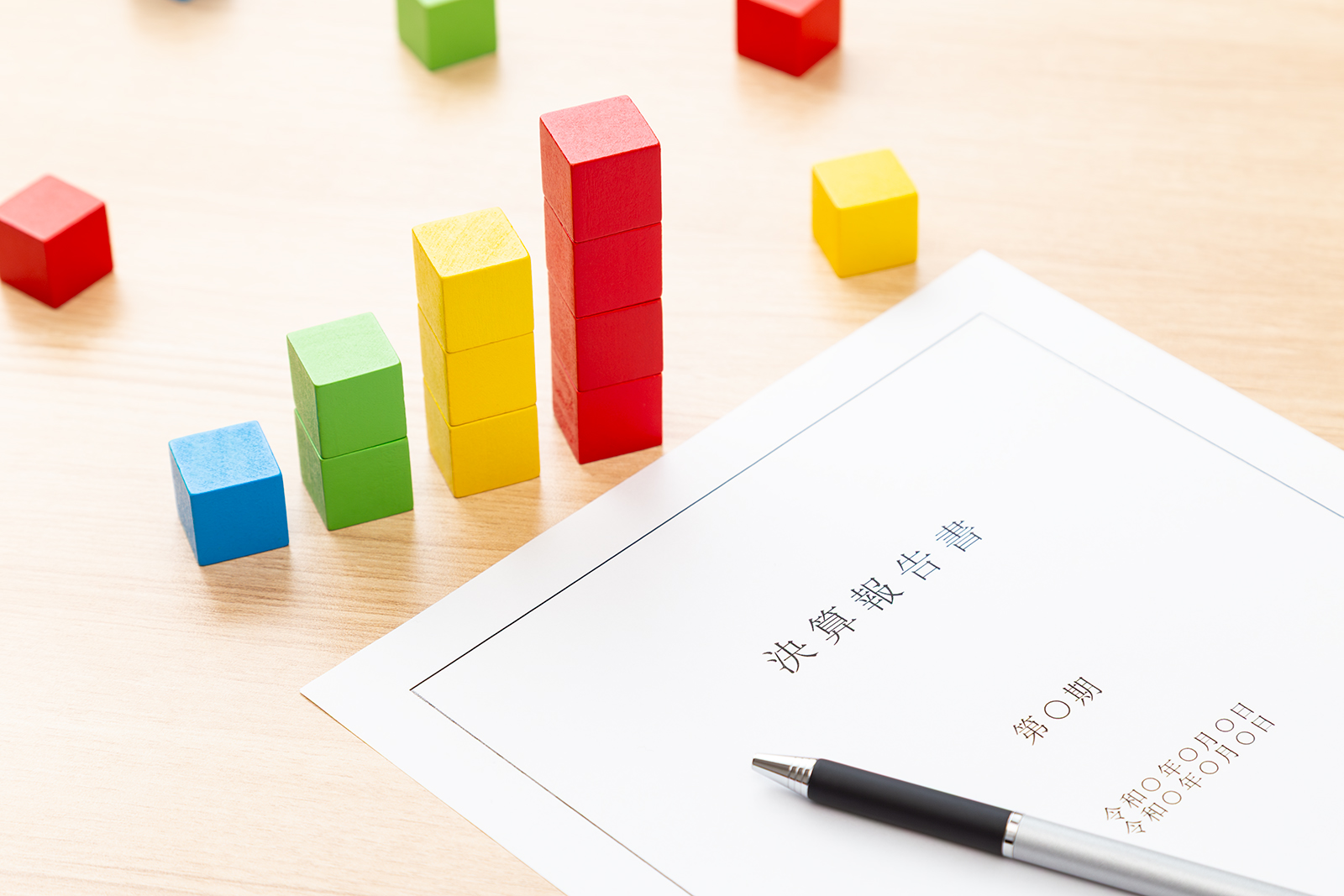 決算報告書とカラフルなブロックで業績を表現するイメージ