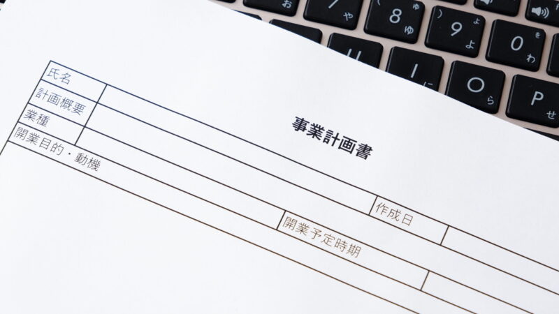 ノートパソコンのキーボードの上に置かれた事業計画書の用紙。補助金申請や開業計画の作成をイメージした写真。