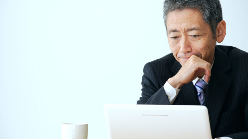 ノートパソコンを見ながら決算資料を確認するスーツ姿の男性経営者。年内の経費や節税対策を検討している様子。