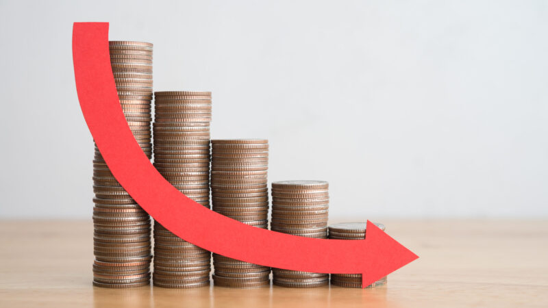 積み重ねた硬貨と下向きの赤い矢印で、売上や利益の減少を示すイメージ