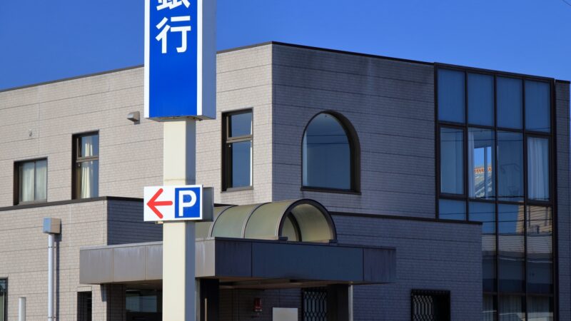 地方銀行の外観と駐車場案内の看板。中小企業の資金調達や銀行融資をイメージした写真。
