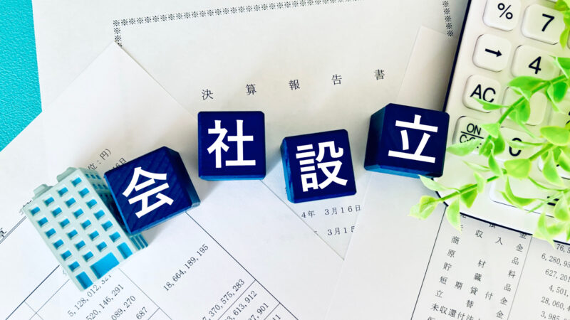 書類と電卓の上に「会社設立」の文字ブロックが並ぶイメージ